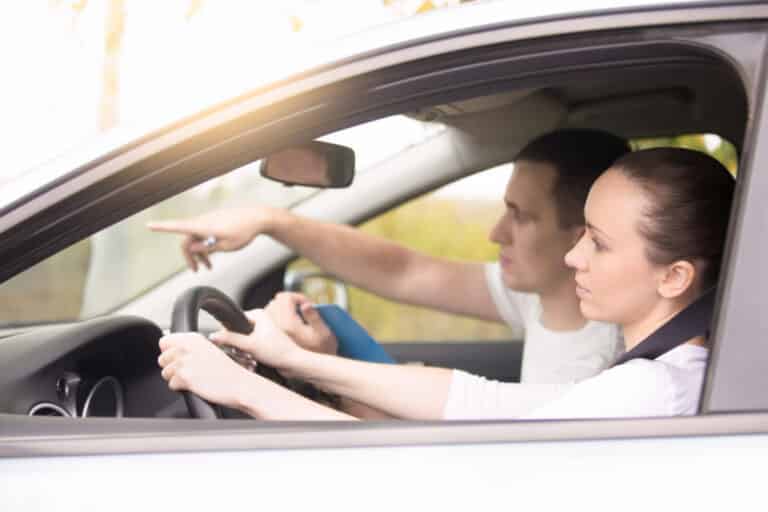 Fahrschülerin am Steuer, der Fahrlehrer zeigt ihr die Richtung