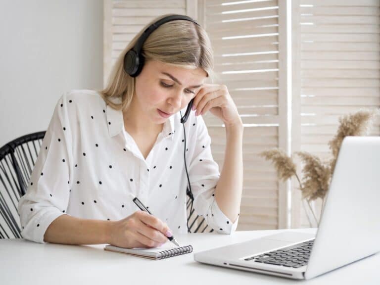 Frau mit Headset lernt am Laptop und schreibt Notizen mit
